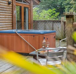 An outdoor space with a hot tub and a table with a glass and bottle at Piran Spa Lodge Pet Perranporth