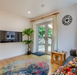 A living room with a television and doors leading to a deck at Poldark Spa Pet Perranporth