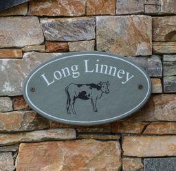 A sign with the name Long Linney and a cow illustration on a stone wall at Long Linney in Bideford