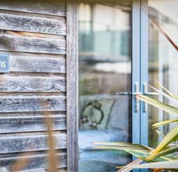 A wooden wall with a sign and glass door at Warrens Spa in Marhamchurch