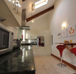 A kitchen with a microwave, cabinets, bar stools, and countertop at Westcotts in Marhamchurch