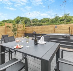 An outdoor dining area with a table and hot tub at Gwari Spa Barn 3.0 in Marhamchurch