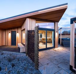 An exterior view of a modern wooden house with a hot tub at Trelowen 3.0 Spa in Marhamchurch