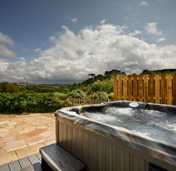 An outdoor area with a hot tub and patio at Whalesborough Cottage Spa in Marhamchurch