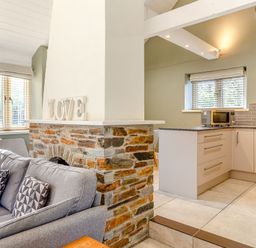 A living room with a sofa and kitchen area at Godolphin Stable Bude