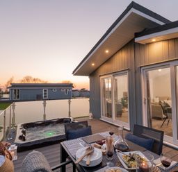 An outdoor deck with a hot tub and dining setup at Mullion 2 Spa (Pet) Bude