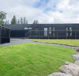 A black building with a wooden railing and grass at Cabin 2.0 Deluxe in Dumfries