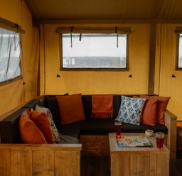 A living room with a sofa, cushions, and drinks at Deluxe Safari Tent in Fair Oak