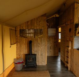 A tent interior with a wood stove and shelves at Deluxe Safari Tent in Fair Oak