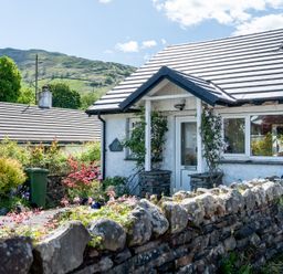 A cottage with a stone wall and flowers outside at Oaks Lodge Cottage Ambleside
