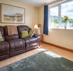 A living room with a sofa, cushions, lamp, and window at Oaks Lodge Cottage in Ambleside