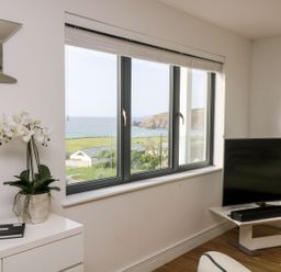 A living room with a television and a window showing a sea view at Praa Waves in Penzance