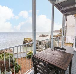 An outdoor balcony with a table and chairs overlooking the ocean at Val's Seaview in Ilfracombe