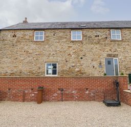 A stone wall building with windows and door in a gravel area at The Granary Durham