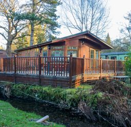 A wooden cabin with a deck near a stream at 6 Waterside in Windermere