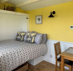 A bedroom with a bed and table in Bluebell Shepherd’s Hut in Llanfairpwllgwyngyll
