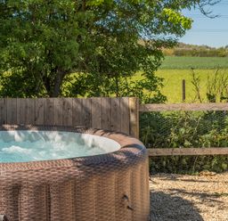A hot tub with a wooden fence and greenery at Cotswold Nights in Ashton Under Hill