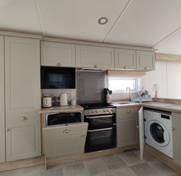 A kitchen with cabinets, stove, microwave, and washing machine at Harbour View in Poole