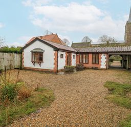 A house with a gravel driveway and a church in the background at The Pantiles in Banham