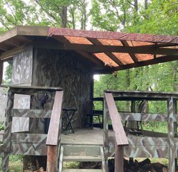 A tree house with a wooden deck and camouflage walls at The Tree House in the Woods Longhope