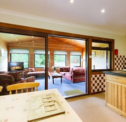 A kitchen with a table and chairs and a view to a living area at Buzzard Lodge in Crianlarich