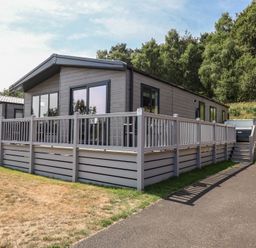 A log cabin with a decking area at Cedar Lodge 3 Bedrooms with hot tub Delamere