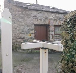 A stone building with a door beside a signpost in Grange-over-Sands