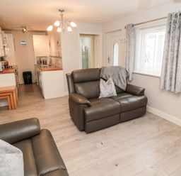 A living room with a sofa and kitchen counter at Primrose Cottage in Chathill