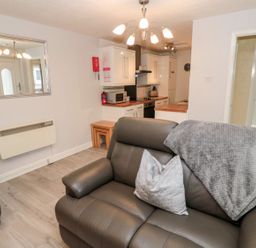 A living room with a sofa and kitchen area at Primrose Cottage in Chathill
