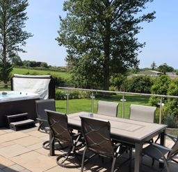 An outdoor area with a hot tub and dining table at Holly Lodge in Lloc near Caerwys