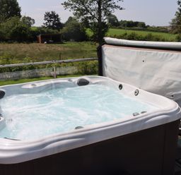 A hot tub on a deck with grass and trees in the background at Pine Lodge in Lloc near Caerwys