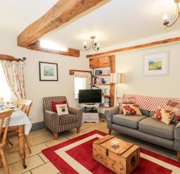 A living room with a gray sofa armchair dining table and wooden beams at Honey Bee Cottage in Staintondale