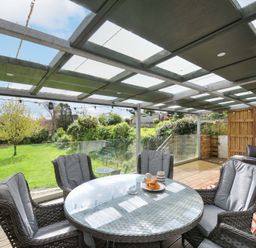 A conservatory with a glass table and chairs overlooking a garden at Porthmeor in Wadebridge