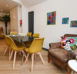 A dining room with a table and chairs, a sofa, and wall art at Still Waters in Weymouth