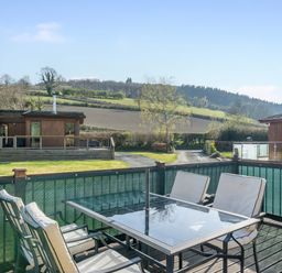 A terrace with chairs and a table overlooking hills at Hazel Lodge in Craven Arms