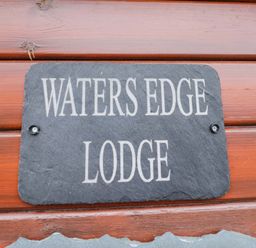 A sign displaying 'WATERS EDGE LODGE' on a wooden structure at Waters Edge Lodge in Windermere