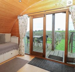 A snug with a couch and sliding door leading to a deck at Vine View near Halesworth