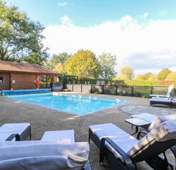 An outdoor swimming pool area with chairs and a cabin at Oldfields in Bury St Edmunds