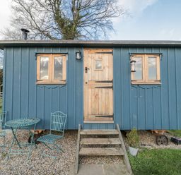 A blue hut with wooden door and outdoor seating at Honeysuckle Hut, Potto Grange Farm, Northallerton