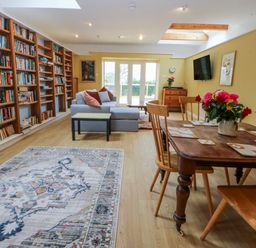 A living room with a bookshelf, sofa, and dining table at Inglewood Bach in Conwy