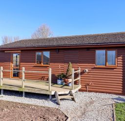 A wooden cabin with a deck and potted plants at Star Carr Lakes