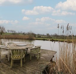 An outdoor space with a table and chairs by the water at The Barn on The Lagoon in Droitwich