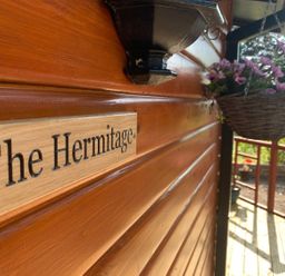 A sign on a wooden building with flowers at The Hermitage Penrith