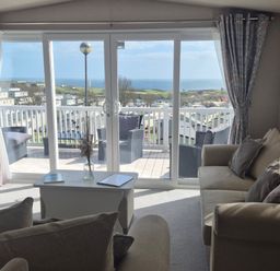 A living room with sliding doors leading to a deck overlooking the sea at 21 Gorse Hill in Exmouth