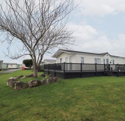 A mobile home with a wooden deck and a tree in the outdoor area at Lily's Lodge in Morecambe
