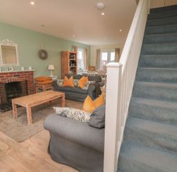 A living room with a fireplace and staircase at Sandy Cove in Chathill