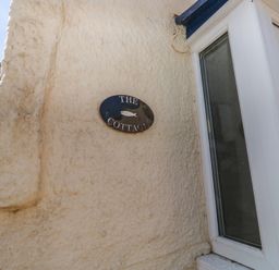 A nameplate on the wall next to a door at The Cottage in Budleigh Salterton