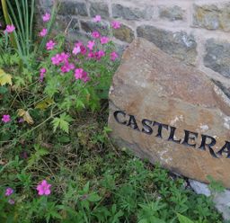 A stone with the name Castlerag surrounded by flowers at Castlerag in Parkend