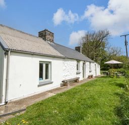 An outdoor area with a cottage, table, and umbrella at Rhos Y Clegyrn Goodwick