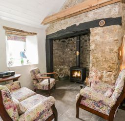A living room with a wood stove and floral armchairs at Rhos Y Clegyrn in Goodwick